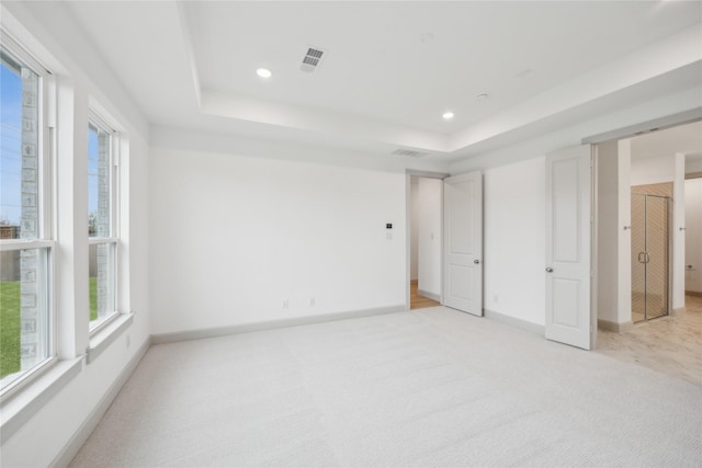 unfurnished bedroom with light colored carpet and a tray ceiling