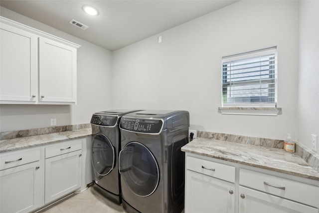 clothes washing area featuring washer and dryer, light tile patterned floors, and cabinets