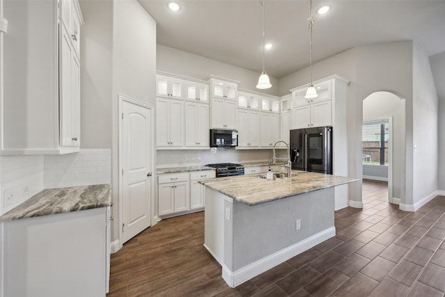 kitchen with appliances with stainless steel finishes, light stone counters, a kitchen island with sink, sink, and white cabinetry