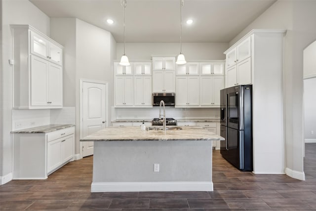 kitchen with light stone countertops, pendant lighting, a kitchen island with sink, white cabinets, and appliances with stainless steel finishes