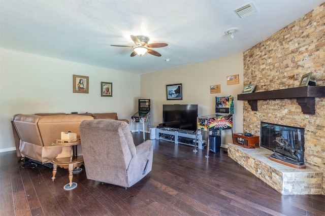 living room with a stone fireplace, visible vents, baseboards, a ceiling fan, and dark wood finished floors