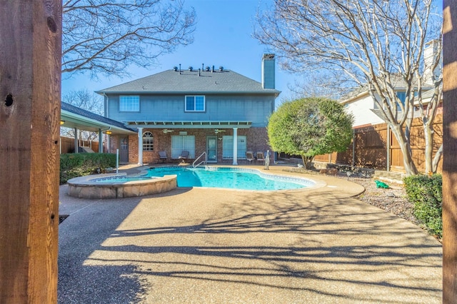 back of property featuring a patio, brick siding, fence, a pool with connected hot tub, and a chimney