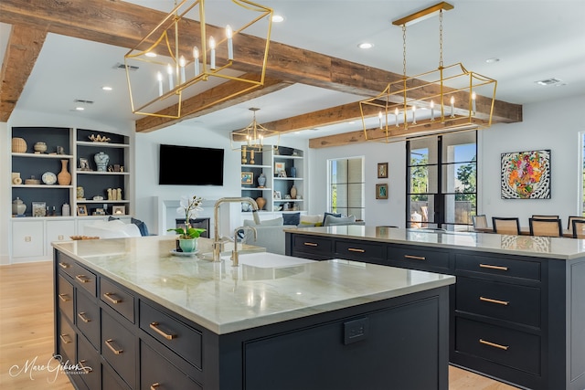 kitchen with pendant lighting, beamed ceiling, sink, light stone counters, and a spacious island