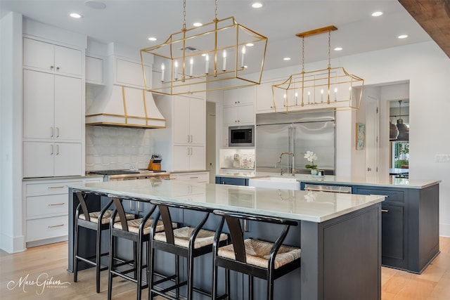 kitchen featuring a spacious island, custom exhaust hood, white cabinets, and built in appliances