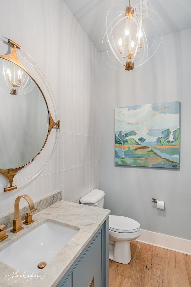 bathroom with toilet, a notable chandelier, wood finished floors, tile walls, and vanity