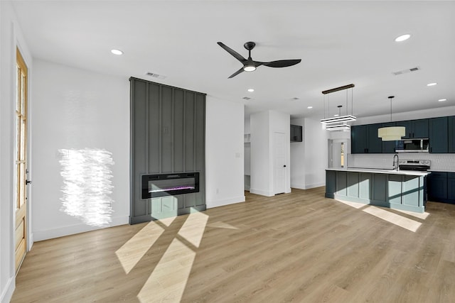 kitchen with decorative backsplash, stainless steel appliances, light hardwood / wood-style flooring, and an island with sink