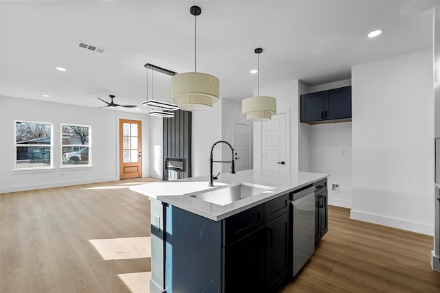 kitchen featuring ceiling fan, sink, hanging light fixtures, stainless steel dishwasher, and a center island with sink