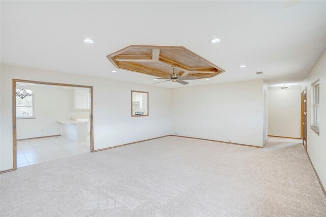 carpeted spare room featuring ceiling fan with notable chandelier and a tray ceiling