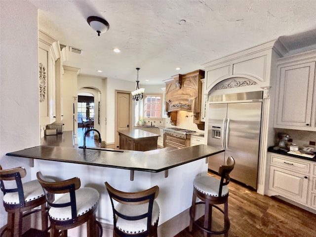 kitchen with premium range hood, sink, built in refrigerator, kitchen peninsula, and pendant lighting