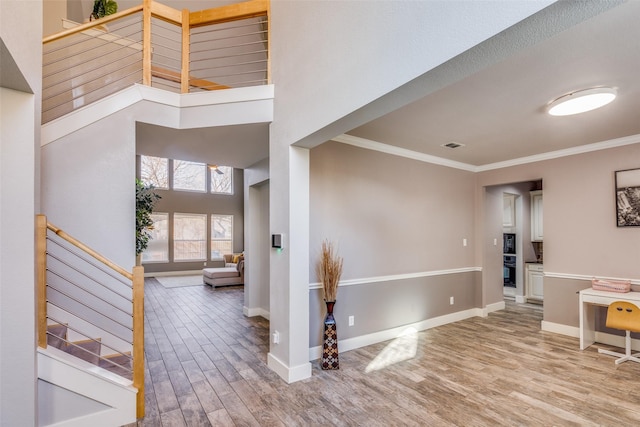 entryway featuring crown molding, a towering ceiling, and light hardwood / wood-style floors