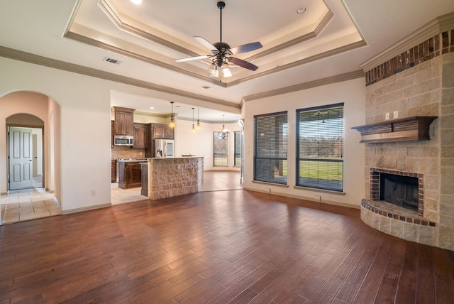 unfurnished living room featuring ceiling fan with notable chandelier, crown molding, dark hardwood / wood-style floors, and a tray ceiling