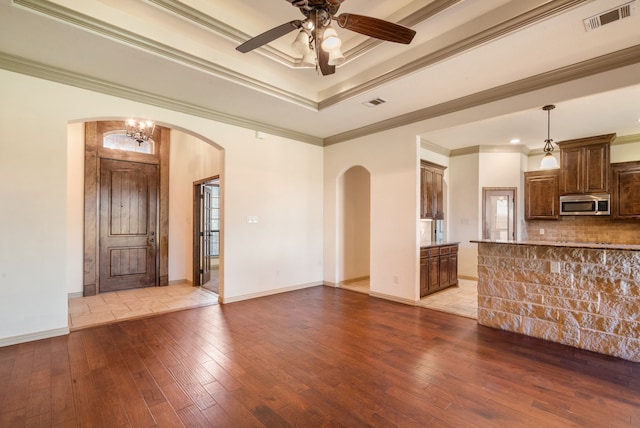 unfurnished living room with ornamental molding, light hardwood / wood-style flooring, ceiling fan with notable chandelier, and a tray ceiling