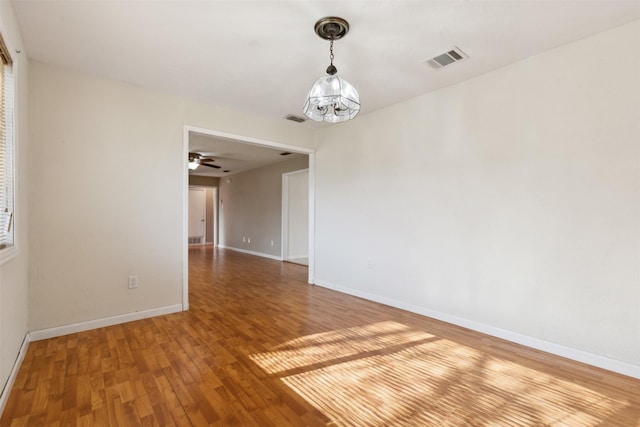 empty room with hardwood / wood-style floors and ceiling fan with notable chandelier