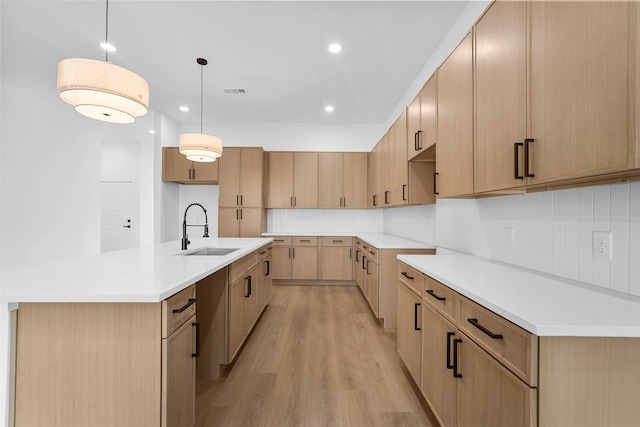 kitchen with decorative light fixtures, light hardwood / wood-style floors, sink, and an island with sink