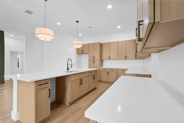 kitchen with a kitchen island with sink, sink, decorative light fixtures, and light brown cabinets