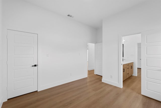 unfurnished bedroom featuring ensuite bath and light hardwood / wood-style floors