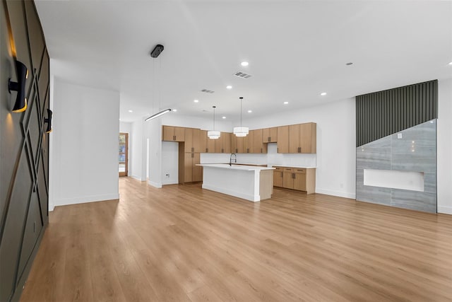 kitchen with sink, a center island with sink, hanging light fixtures, and light wood-type flooring