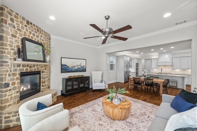 living room featuring dark hardwood / wood-style flooring, ornamental molding, ceiling fan, sink, and a fireplace