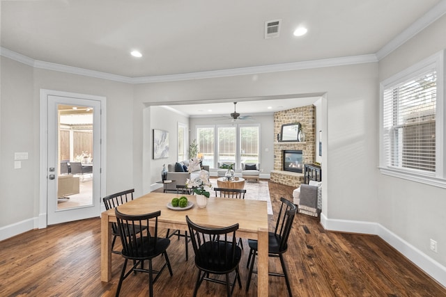 dining area featuring ceiling fan, ornamental molding, dark wood-type flooring, and a brick fireplace