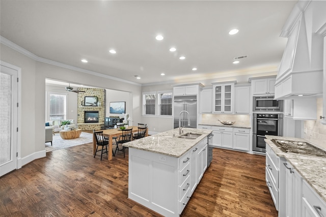 kitchen with backsplash, built in appliances, white cabinetry, and an island with sink