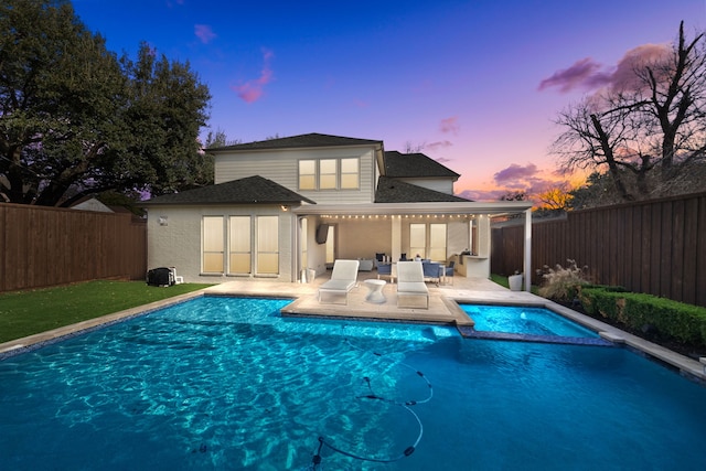 back house at dusk with a pool with hot tub