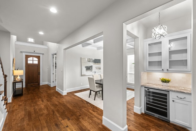 entrance foyer featuring dark wood-type flooring, coffered ceiling, beam ceiling, beverage cooler, and a chandelier