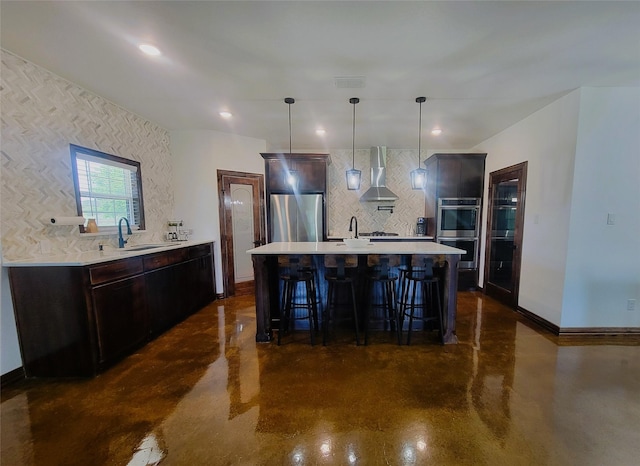 kitchen featuring appliances with stainless steel finishes, sink, wall chimney range hood, pendant lighting, and a breakfast bar area