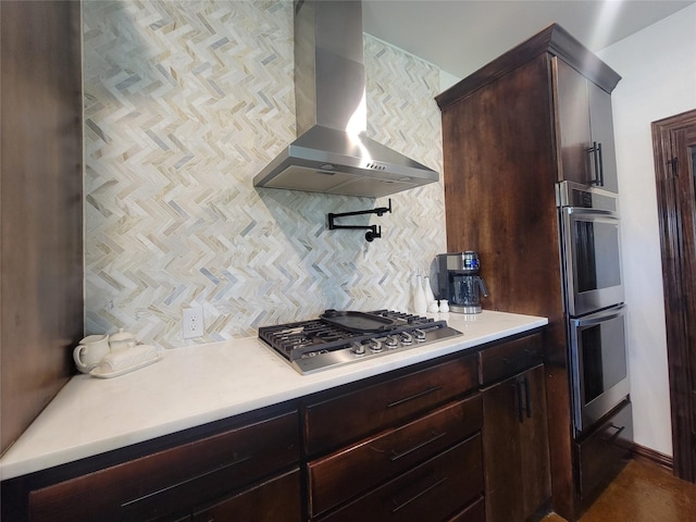 kitchen with decorative backsplash, dark brown cabinetry, wall chimney range hood, and appliances with stainless steel finishes