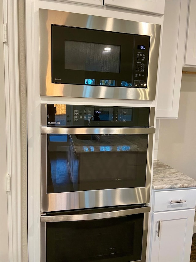 room details featuring stainless steel double oven, light stone countertops, built in microwave, and white cabinetry