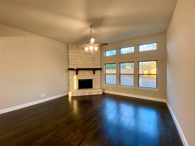 unfurnished living room featuring ceiling fan, dark wood-type flooring, and a stone fireplace