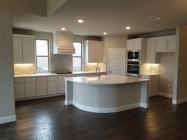 kitchen with custom exhaust hood, dark hardwood / wood-style floors, stainless steel appliances, a kitchen island with sink, and white cabinetry