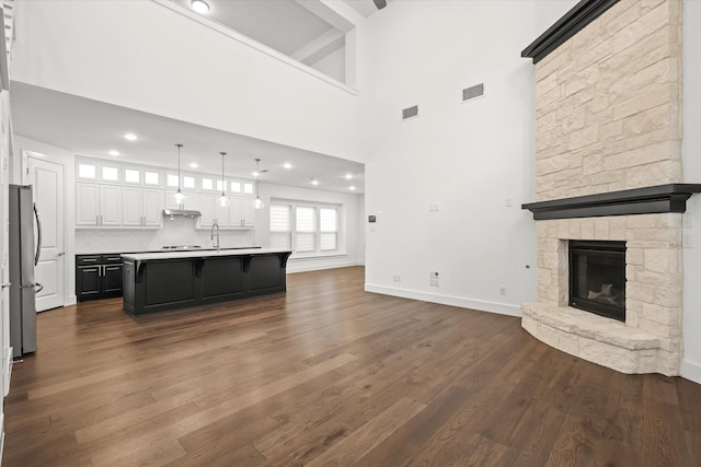 living room with a high ceiling, a stone fireplace, dark wood-type flooring, and sink