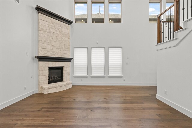 unfurnished living room with a stone fireplace, a towering ceiling, and dark wood-type flooring