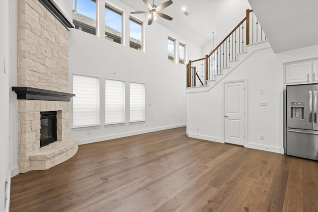 unfurnished living room with wood-type flooring, a towering ceiling, a stone fireplace, and ceiling fan