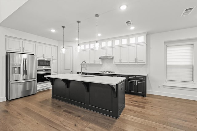 kitchen with white cabinetry, sink, tasteful backsplash, a center island with sink, and appliances with stainless steel finishes