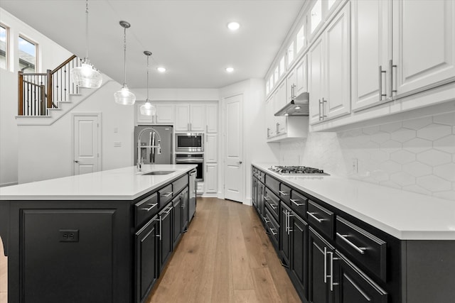 kitchen with tasteful backsplash, a center island with sink, white cabinets, and appliances with stainless steel finishes