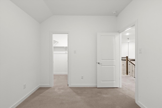 unfurnished bedroom featuring vaulted ceiling, light colored carpet, a spacious closet, and a closet