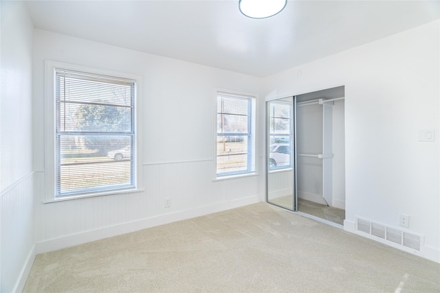 unfurnished bedroom with multiple windows, light carpet, and a closet