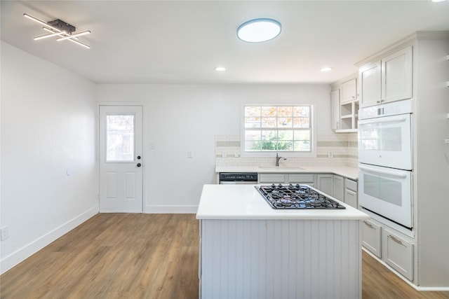 kitchen with white double oven, sink, a center island, stainless steel gas stovetop, and decorative backsplash