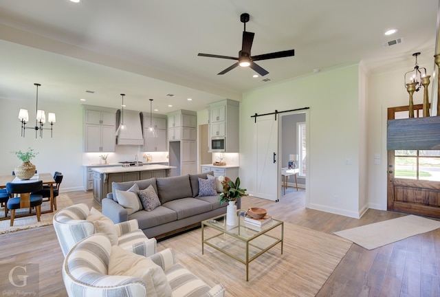 living room with ceiling fan with notable chandelier, sink, a barn door, ornamental molding, and light hardwood / wood-style floors