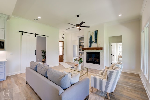 living room featuring ceiling fan, crown molding, a barn door, light hardwood / wood-style flooring, and a premium fireplace