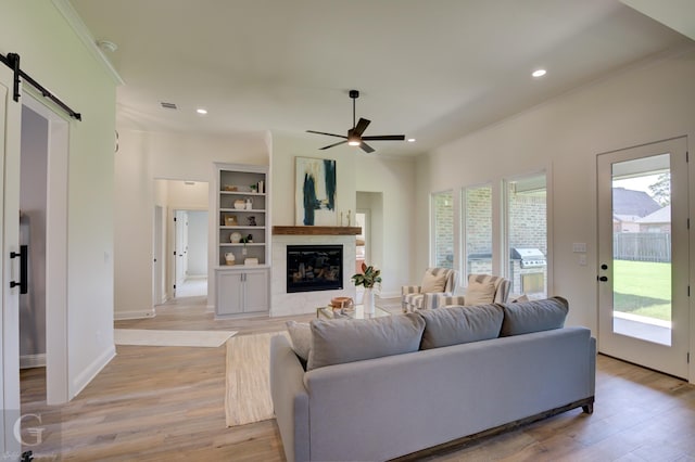 living room featuring built in shelves, light hardwood / wood-style floors, a wealth of natural light, and ceiling fan