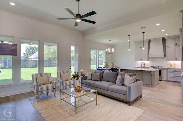 living room featuring ceiling fan with notable chandelier, light hardwood / wood-style floors, plenty of natural light, and sink