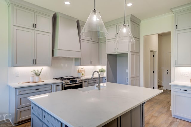 kitchen with tasteful backsplash, stainless steel gas range oven, custom exhaust hood, decorative light fixtures, and a center island with sink