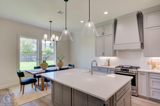 kitchen featuring sink, stainless steel range oven, gray cabinets, a kitchen island with sink, and custom exhaust hood