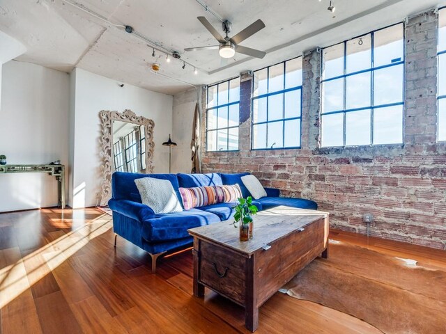 living room featuring wood-type flooring, rail lighting, ceiling fan, and brick wall