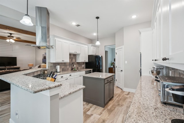 kitchen featuring black refrigerator, ventilation hood, a kitchen island, pendant lighting, and white cabinetry