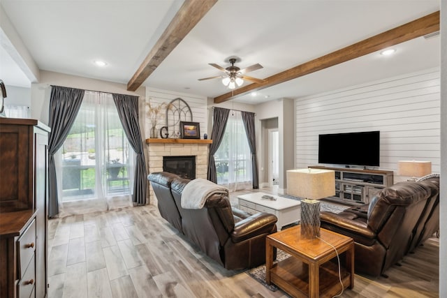 living room with ceiling fan, wooden walls, beam ceiling, light hardwood / wood-style flooring, and a fireplace