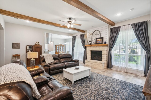 living room featuring a stone fireplace, ceiling fan, and beamed ceiling