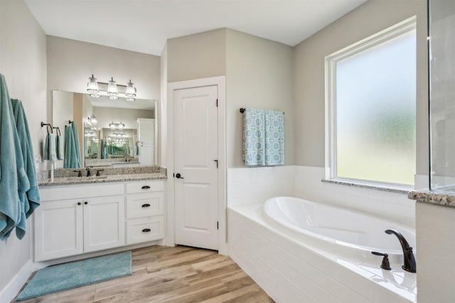 bathroom with tiled tub, vanity, and wood-type flooring